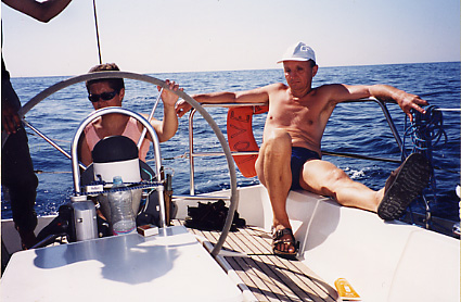 Photo de Michel assis  l'arrire du voilier et Claudine  la barre par une chaude journe en pleine mer.
